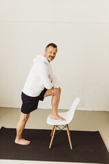 Senior man using a chair to do stretch exercises in a home gym