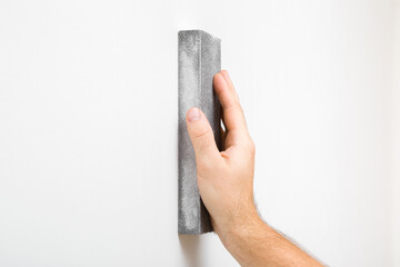 Young adult man hand polishing white wall with sanding sponge. Closeup. Side view.