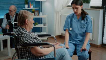 Fototapeta premium Disabled senior woman in nursing home talking to nurse for healthcare examination and checkup. Medical assistant giving advice for recovery to elder patient with disability in wheelchair.