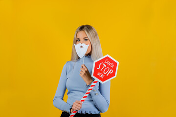 Beautiful girl celebrating and having fun at a party with photo props like beard, and stop signal on yellow background. New year and fun party concept