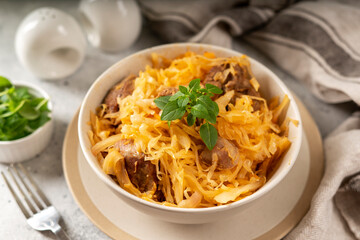Braised (stewed) cabbage or bigos with turkey meat in a ceramic plate on a light culinary background. Traditional Polish dish