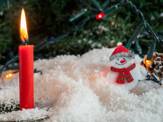 Candle and a sn on decorative snow under a Christmas tree