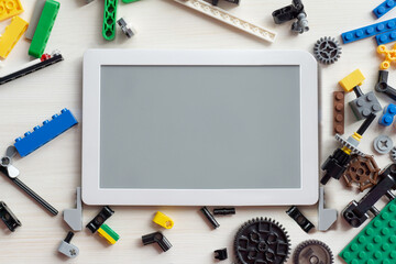 Top view of tablet layout, surrounded by various details, for children's design, on white wooden background. Concept of online courses in robotics, electronics, and science