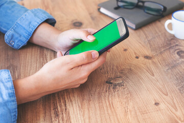 Cropped shot top view of businesswoman hands using smartphone mockup at the wooden office desk. Blank screen mobile phone for graphic display montage