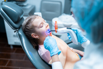  dentist providing tooth restoration and filling with curing polymerization UV lamp for little girl 