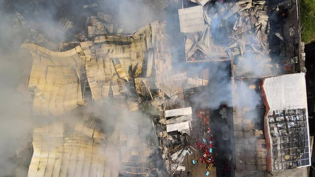Aerial view of ruined building on fire with collapsed roof and rising dark smoke