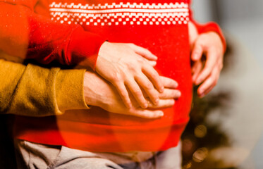 Husband hugs his wife pregnant belly. Christmas atmosphere. Close-up of hands and abdomen