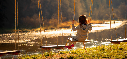 Beautiful young child girl having fun on a swing outdoor against on the background of the river and mountains. Happy childhood, vacation and holiday concept.
