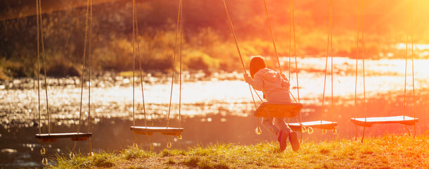 Portrait of young girl having fun on a swing outdoor against on the background of the river in sun...