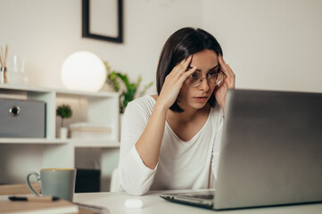 Woman feeling tired and stressed while using a laptop and working from home