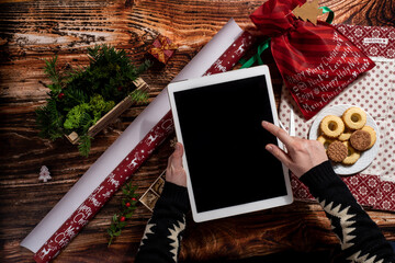 Top view of woman's hands holding digital tablet while wrapping Christmas presents