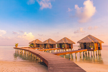 Sunset on Maldives island, luxury water villas resort hotel and wooden pier. Colorful sky and clouds and beach background for summer vacation holiday, traveling destination. Paradise sunset landscape