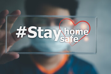 Fototapeta na wymiar Young man in medical mask holding sign with stay home stay safe text. Social media campaign for coronavirus prevention
