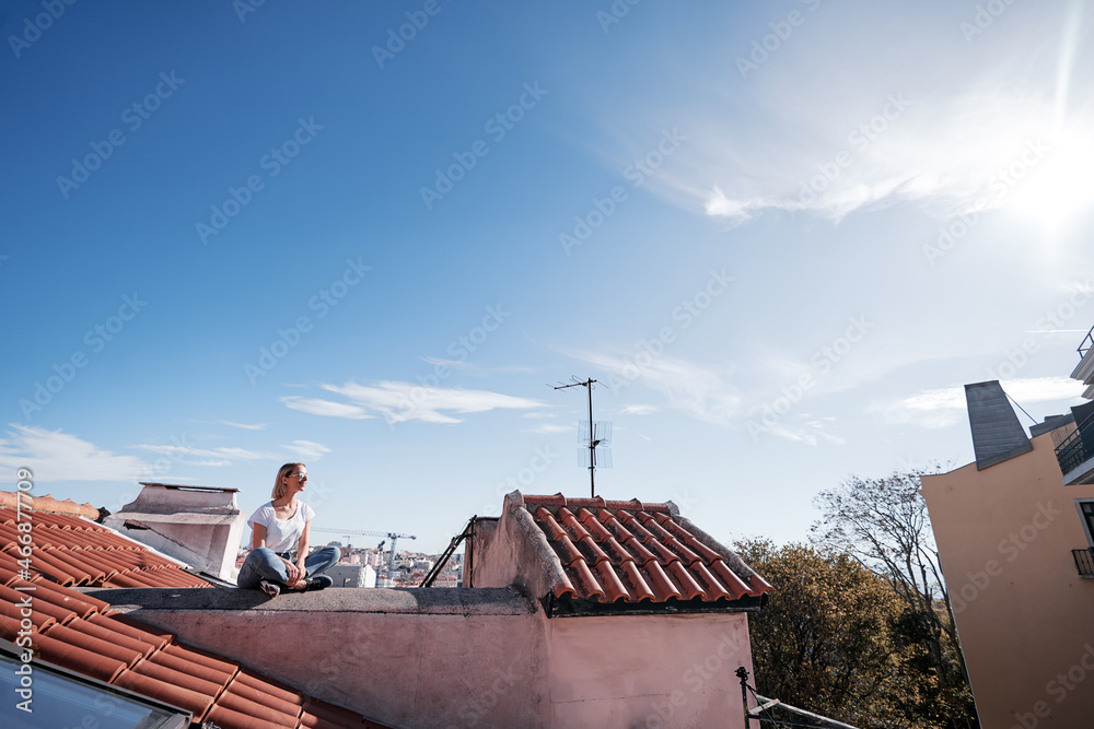 Wall mural Happy young woman sitting on red tiled roof.