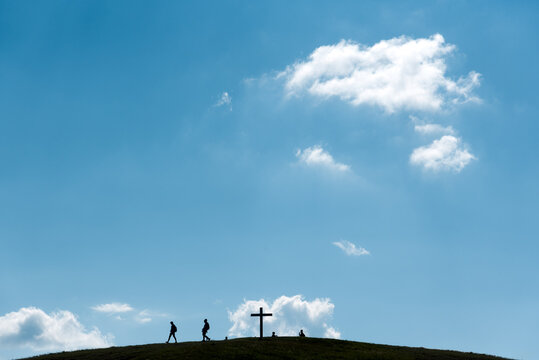 Silhouettes of walking people and big cross on a hill under a blue sky