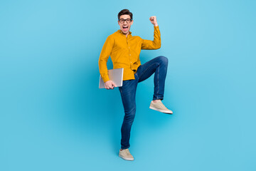 Photo of champion guy hold pc celebrate victory wear yellow shirt jeans sneakers isolated blue...