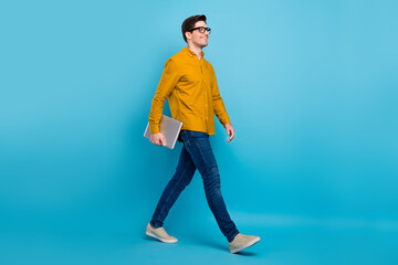 Profile photo of guy walk hold netbook enjoy stroll wear yellow shirt jeans shoes isolated blue...
