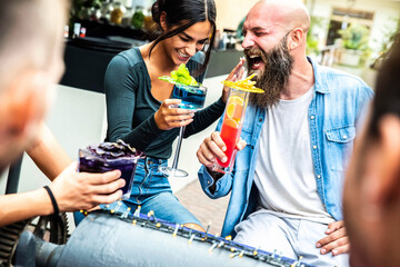 Laughing friends cheering drinks at lounge bar restaurant - Diverse young  people having party drinking cocktails outdoors - Funny multiracial couple smiling making joke together outside