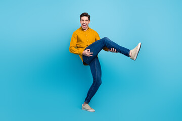 Fototapeta na wymiar Photo of funky inspired guy play imaginary guitar raise leg wear yellow shirt jeans shoes isolated blue color background