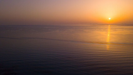 Obraz premium Peaceful seascape landscape aerial view of calm ocean sea water during sunset or sunrise time. Orange and colorful sky and waves. Travel destination amazing place and moments concept