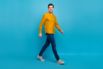 Photo of cheerful positive handsome guy walk go wear yellow shirt jeans sneakers isolated blue color background