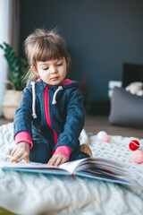 little girl reading a book sitting on a woolen blanket