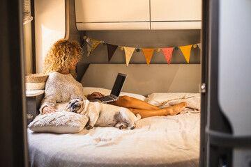 Attractive woman have relax inside van camper laying on bed and using laptop computer connection. Adorable dog sleeping near her. Female independent people digital nomad lifestyle - Powered by Adobe