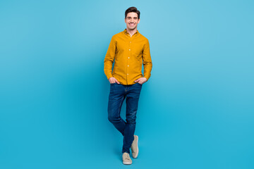 Photo of positive boyfriend guy hand pocket posing wear yellow shirt jeans sneakers isolated blue color background