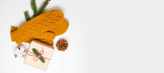 Christmas holiday composition of mustard knitted mittens with xmas gift box and pine cone decor on white background with copy space