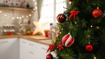 Stylish room interior with beautiful Christmas tree and decorative kitchen in apartment. focus side view on xmas tree full of red balls decor on celebration of holiday with blurred background indoors