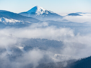 High mountain peak raising above foggy valley in winter.