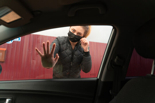 A girl in a medical mask looks at the camera. Hand on car glass