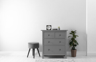 Elegant room interior with stylish chest of drawers, pouf and houseplant
