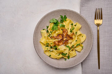 Top view Italian pasta pappardelle with mushrooms chanterelles, cheese and parsley on plate with golden fork and napkin
