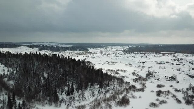Aerial shot in movement of snowed hills with green spruces when it's snowing