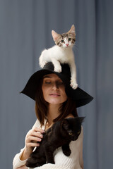 white kitten is sitting on the hat with a large brim head of a young woman. She holds her hands black kitten.