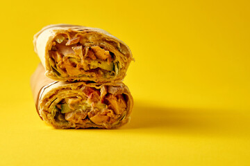 Large shawarma with meat and vegetables, wrapped in foil on a yellow background. Close-up,...