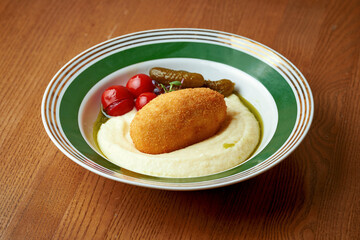 Chicken Kiev with tomatoes, cucumber and mashed potatoes in a plate on a wooden background