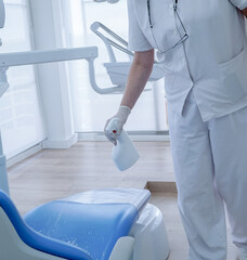 auxiliar de clínica de odontología con guantes de látex y ropa blanca desinfecta la camilla del paciente después de una intervención  - obrazy, fototapety, plakaty