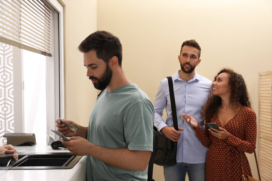 Man with money and other people in line at cash department window. Currency exchange - Powered by Adobe