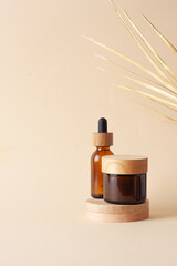 Cosmetic skin care products with wood podium and palm leaf on pastel beige background. Close up,...