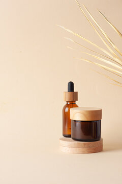 Cosmetic skin care products with wood podium and palm leaf on pastel beige background. Close up, copy space