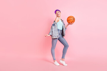 Full size profile photo of funny sporty lady hold ball look empty space wear jeans shirt cap isolated on pink background