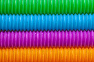 Rainbow colored anti-stress fidget pop tube sensory toy background. Close-up of trendy game with popular plastic flexible bright corrugated pipe.