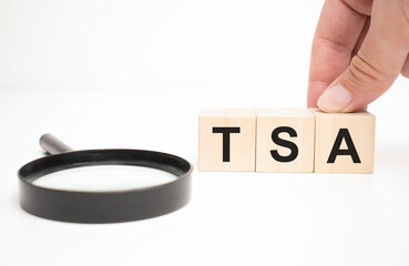 tsa text wooden cube blocks and hand holding magnifying glass on table background.