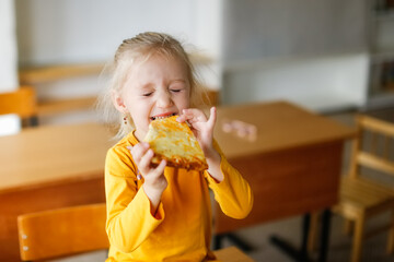 Cute caucasian girl child blonde eating a slice of pizza with cheese, a snack at school, junk food...
