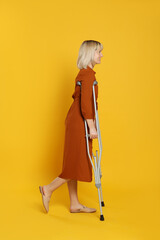 Full length portrait of woman with crutches on yellow background
