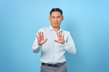 Naklejka premium Portrait of angry young handsome businessman doing stop gesture with hand palms on blue background