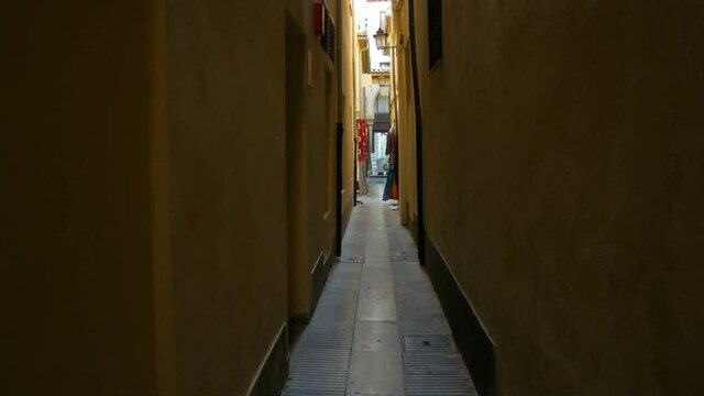 Dark narrow alley in the historical centre of Granada, Andalusia, Spain. Dark walls on both sides. Commercial street at the vanishing point.