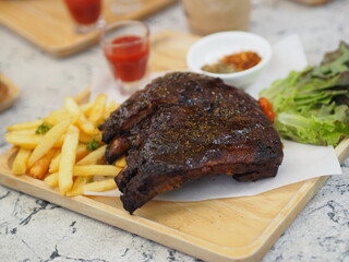 Pork Spareribs BBQ, Barbeque Pork Ribs with french fries vegetable salad, tomato sauce in a clear glass on wooden tray, food